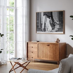 K&ouml;nnte beinhalten: Ein Holzschr&auml;nkchen mit einer geflochtenen Rattan-T&uuml;r und drei Schubladen. Der Schrank steht in einem Wohnzimmer mit einem wei&szlig;en Sofa, einem Glas-Couchtisch und einem Schwarzwei&szlig;foto eines Paares und einer Katze, das an der Wand h&auml;ngt.