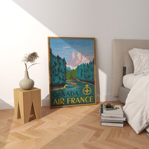 May include: A vintage travel poster for Air France featuring a scenic landscape of mountains, trees, and a river. The poster is framed in gold and has the text "Canada Air France" at the bottom.