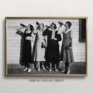 May include: Black and white vintage photograph of four women in dresses holding bottles and posing in front of a wooden wall.