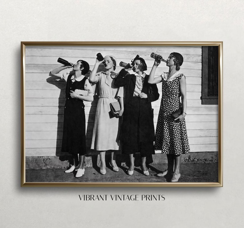 May include: Black and white vintage photograph of four women in dresses holding bottles and posing in front of a wooden wall.