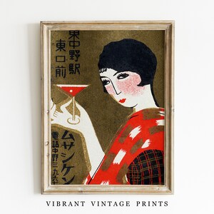 K&ouml;nnte beinhalten: Vintage Art-Deco-Druck mit einer Frau, die einen Cocktail h&auml;lt. Das Kunstwerk hat ein Gold- und Rot-Farbschema mit japanischem Text. Der Druck ist gerahmt und enth&auml;lt den Text "VIBRANT VINTAGE PRINTS".