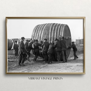 Puede incluir: Un grupo de hombres con ropa de principios del siglo XX empujan un gran barril de madera por un camino de tierra.