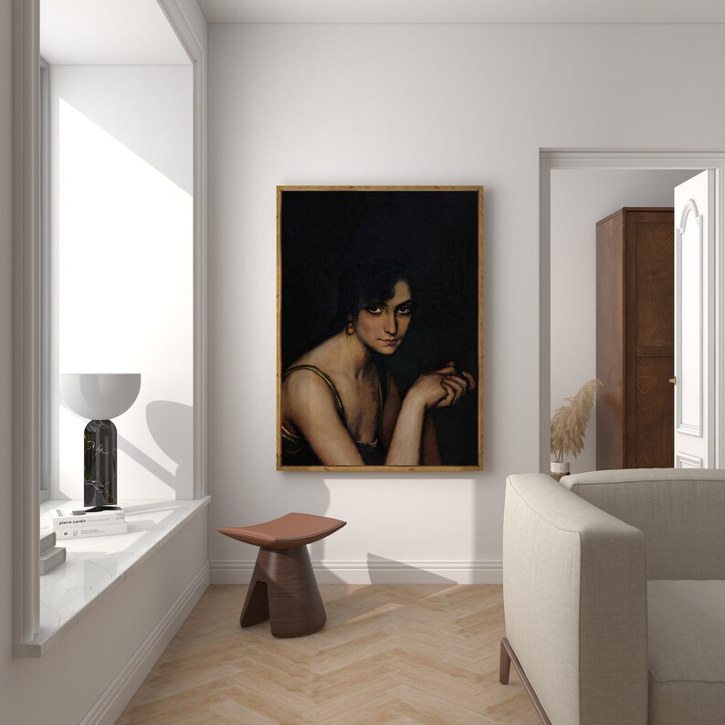 Pode incluir: Um retrato emoldurado de uma mulher com cabelo escuro e um vestido verde, sobre um fundo escuro. A pintura est&aacute; pendurada em uma parede branca em uma sala com piso de madeira e um sof&aacute; branco.