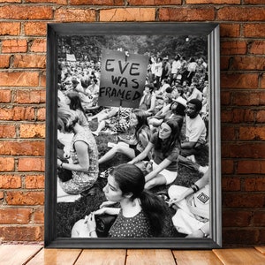 Puede incluir: Fotograf&iacute;a en blanco y negro de una protesta con un cartel que dice "Eve Was Framed". La foto muestra a un grupo de personas sentadas en la hierba, algunas sosteniendo carteles.
