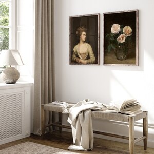 May include: Two framed vintage art prints. One depicts a woman in a yellow dress, the other a still life of pink roses in a glass vase. A woven bench with a blanket and open book sits below the artwork.