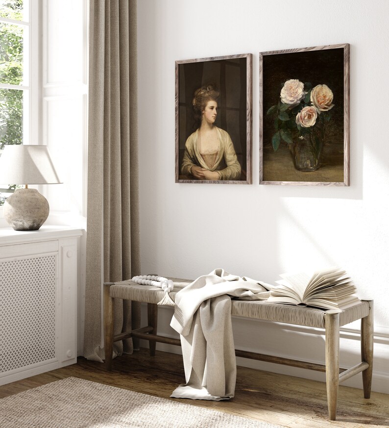 May include: Two framed vintage art prints. One depicts a woman in a yellow dress, the other a still life of pink roses in a glass vase. A woven bench with a blanket and open book sits below the artwork.