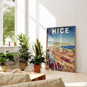 Puede incluir: Un p&oacute;ster de viaje vintage enmarcado con la palabra "NICE". El p&oacute;ster representa una escena costera con palmeras, coches y una mujer con un vestido azul. Varias plantas en macetas est&aacute;n en primer plano, en una habitaci&oacute;n.