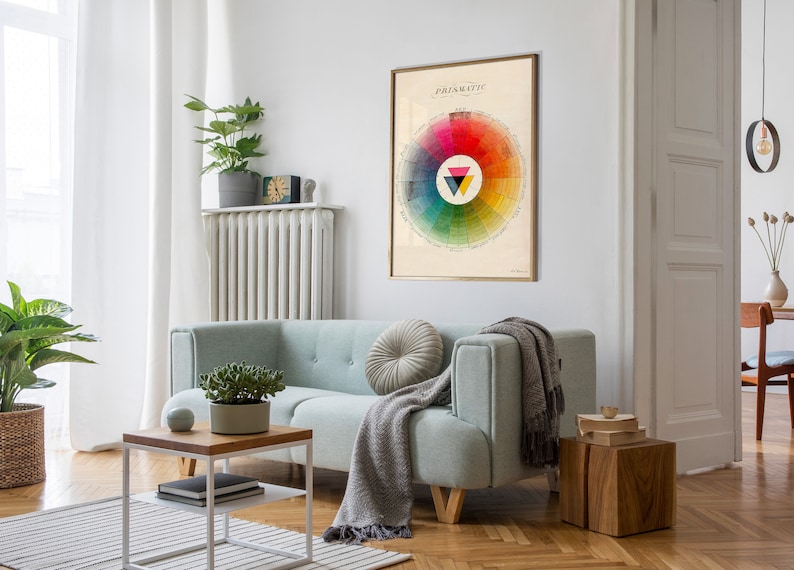 K&ouml;nnte beinhalten: Ein Vintage-Farbkreis-Poster mit dem Titel "Prismatic" h&auml;ngt an einer wei&szlig;en Wand in einem Wohnzimmer. Das Poster zeigt einen kreisf&ouml;rmigen Farbkreis mit einem Dreieck in der Mitte. Der Raum ist mit einem hellblauen Sofa, einem Holz-Couchtisch und einer Topfpflanze dekoriert.