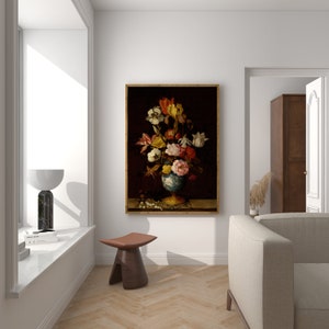 May include: A framed floral still life painting. The artwork features a vibrant bouquet of flowers in a blue and gold vase against a dark background. The painting is displayed in a bright, modern room with a window and a small wooden stool.