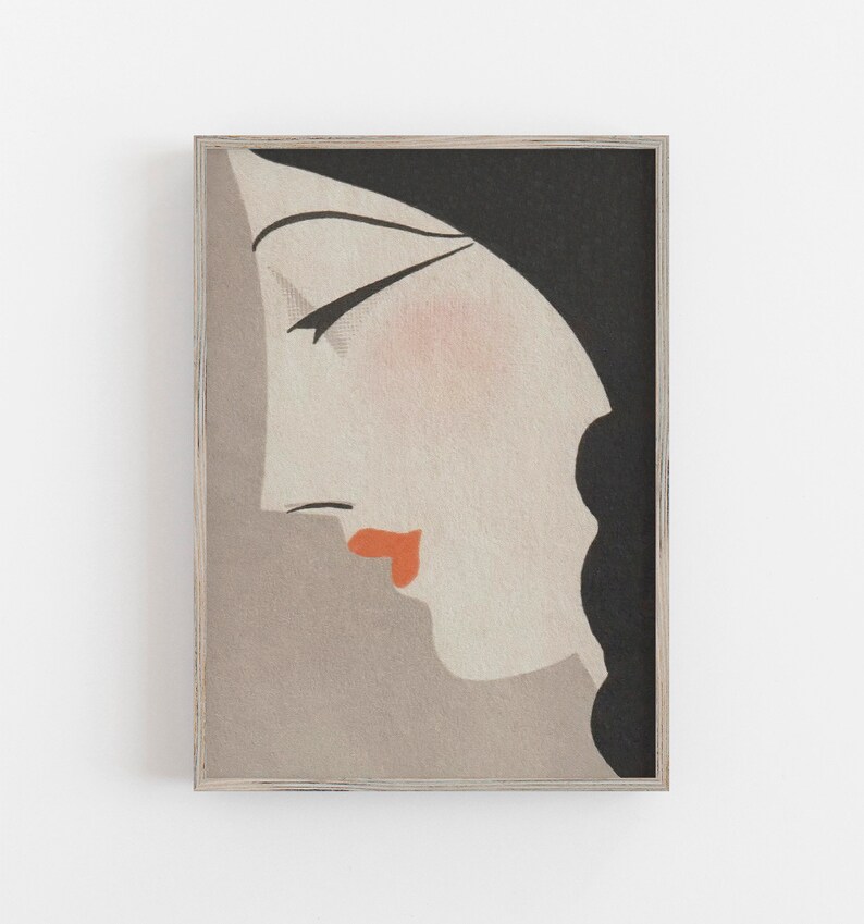 May include: Art Deco style print featuring a woman's profile in shades of gray, black, and peach. The woman's lips are a vibrant orange, and the artwork is framed in a light wood frame. A stylish piece of wall art.