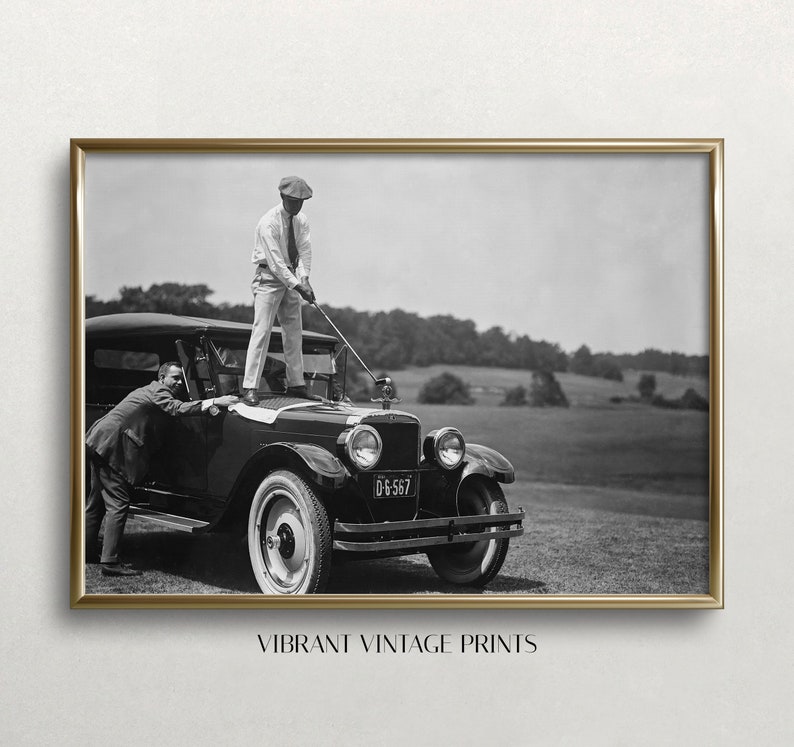 Op de afbeelding: Een zwart-witte vintage foto van twee mannen die golfen. Een man staat op de motorkap van een vintage auto en houdt een golfclub vast, terwijl de andere man op de grond staat en een golfclub vasthoudt. De auto heeft een kentekenplaat met de tekst "D-6567".