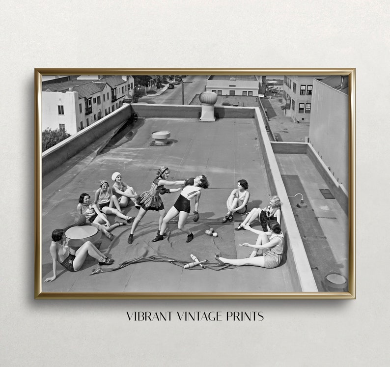 Puede incluir: Una impresi&oacute;n vintage en blanco y negro enmarcada, que muestra a mujeres en una azotea. Algunas boxean, otras observan. La impresi&oacute;n tiene un marco dorado, con el texto "VIBRANT VINTAGE PRINTS" en la parte inferior. El fondo muestra edificios.