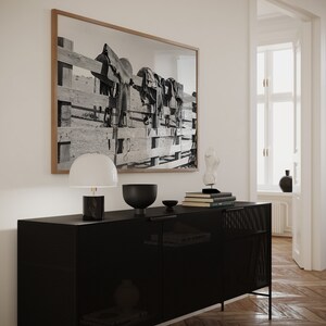 K&ouml;nnte beinhalten: Ein schwarzer Metallschrank mit einer Mesh-Front und zwei T&uuml;ren. Der Schrank steht auf einem Holzboden. Eine wei&szlig;e Lampe mit schwarzem Fu&szlig; steht auf dem Schrank, zusammen mit einer schwarzen Schale und einem Stapel B&uuml;cher. Ein gerahmtes Schwarzwei&szlig;foto von S&auml;tteln, die an einem Zaun h&auml;ngen, befindet sich an der Wand hinter dem Schrank.