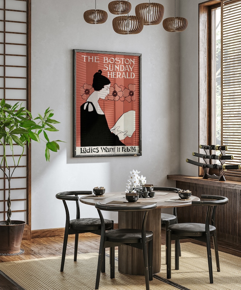 May include: A framed vintage poster for The Boston Sunday Herald, featuring a woman reading, with text "Ladies Want it Feb 24". The poster hangs above a round wooden dining table with four black chairs. The room has a Japanese-inspired design.