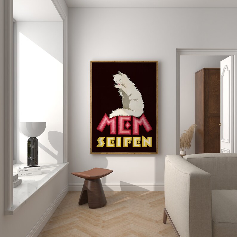 May include: A framed art print featuring a white cat grooming itself, set against a dark background. The artwork includes the text "MEM SEIFEN" in pink and yellow. The print is displayed in a well-lit room with a modern aesthetic.