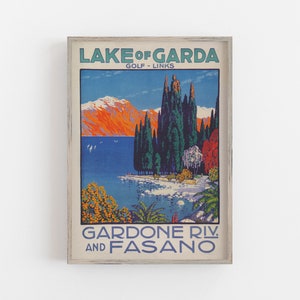 May include: Framed vintage travel poster for Lake Garda, Italy. The artwork features a scenic view of the lake with mountains, trees, and the text "LAKE OF GARDA" and "GARDONE RIV. AND FASANO". The poster has a distressed, aged look.