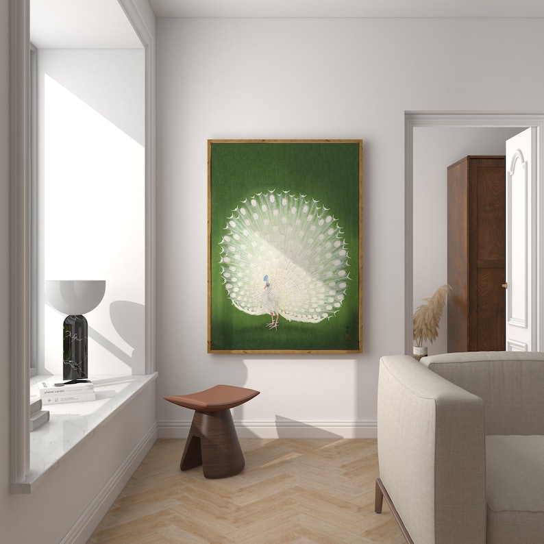 Op de afbeelding: Een ingelijst schilderij van een witte pauw met zijn staartveren uitgespreid tegen een groene achtergrond. Het schilderij hangt aan een witte muur in een woonkamer.
