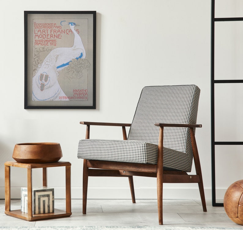 Op de afbeelding: Een moderne woonkamersc&egrave;ne met een ingelijste kunstprint, een stoel met hondenpoottjes en een houten bijzettafel. De kunstprint heeft een pauwenillustratie met tekst. Een houten kom en decoratieve dozen staan op de bijzettafel.