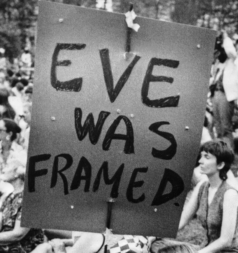 Puede incluir: Fotograf&iacute;a en blanco y negro de un cartel de protesta con el texto "Eve was framed". Una persona est&aacute; sentada en el fondo.