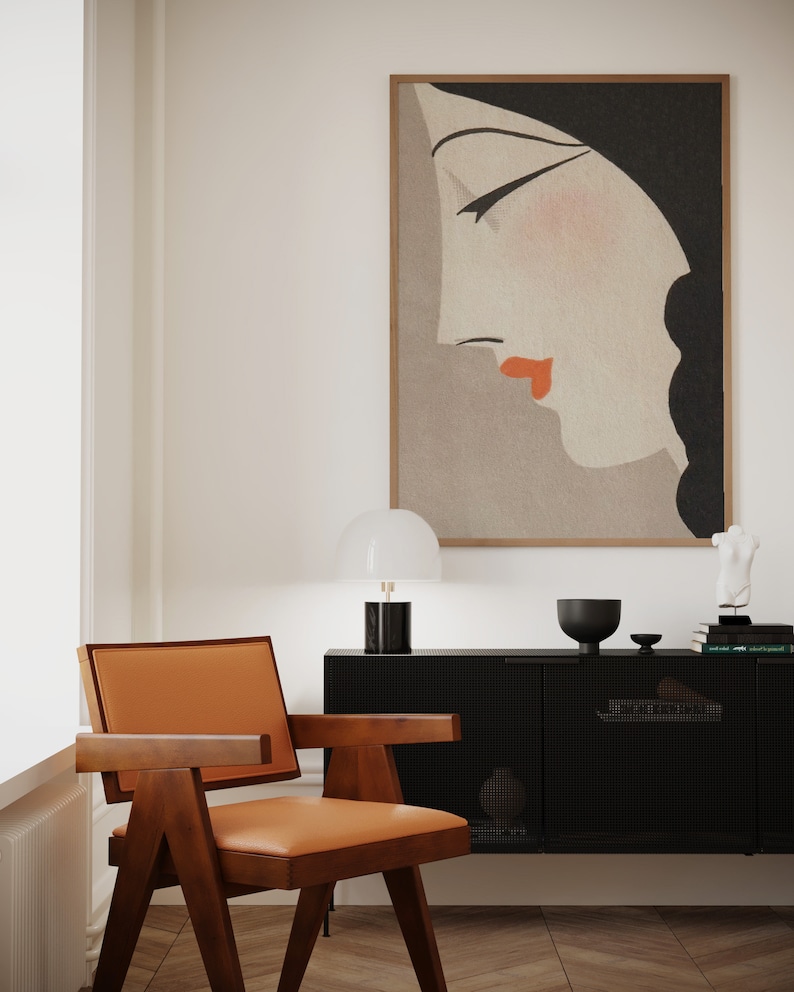May include: A mid-century modern interior featuring a wooden chair with an orange leather seat, a black cabinet, and a framed artwork of a woman's profile. A white lamp and decorative items sit atop the cabinet.