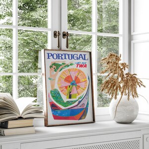 May include: Vintage travel poster advertising a trip to Portugal with TWA airlines. The poster features a colorful illustration of a mermaid with a windmill in the background. The text "FLY TWA" is in the upper right corner.