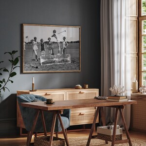 May include: A black and white photograph of five women playing golf on a green course. The women are wearing 1920s clothing and are standing on a block of ice. The photograph is framed in a wooden frame and is hanging on a dark gray wall.