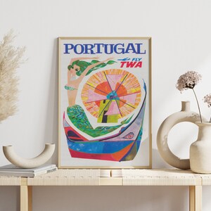 May include: Vintage travel poster advertising flights to Portugal with TWA. The poster features a colorful illustration of a mermaid in a boat with a windmill in the background. The text "PORTUGAL FLY TWA" is printed in blue and red.