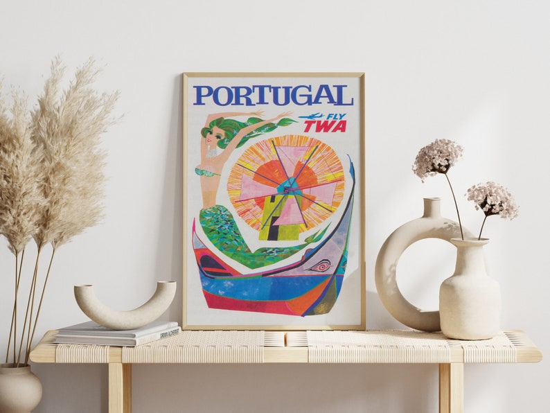 May include: Vintage travel poster advertising flights to Portugal with TWA. The poster features a colorful illustration of a mermaid in a boat with a windmill in the background. The text "PORTUGAL FLY TWA" is printed in blue and red.