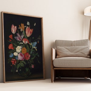 K&ouml;nnte beinhalten: Gerahmtes Blumenstillleben mit dunklem Hintergrund und einem lebendigen Strau&szlig; aus Tulpen, Rosen und anderen Blumen. Das Kunstwerk wird neben einem modernen Sessel mit gemustertem Kissen pr&auml;sentiert.