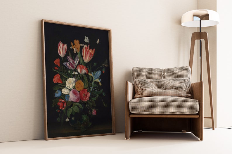 K&ouml;nnte beinhalten: Gerahmtes Blumenstillleben mit dunklem Hintergrund und einem lebendigen Strau&szlig; aus Tulpen, Rosen und anderen Blumen. Das Kunstwerk wird neben einem modernen Sessel mit gemustertem Kissen pr&auml;sentiert.