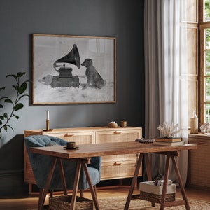 May include: A black and white photograph of a dog listening to a vintage gramophone. The dog is sitting in the snow and the gramophone is playing music. The photo is framed and hanging on a dark blue wall.