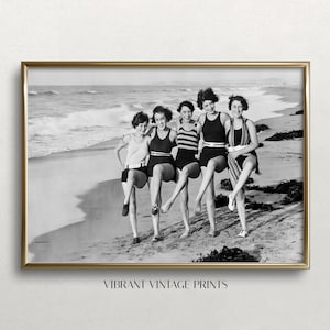 May include: A black and white framed wall art print featuring five individuals in vintage swimsuits standing on a sandy beach with one leg raised. The text VIBRANT VINTAGE PRINTS is centred at the bottom of the image within the frame.