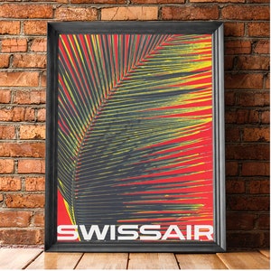 May include: Framed vintage Swissair travel poster. The poster features a large palm leaf in yellow and dark gray against a red background. The word "SWISSAIR" is printed in white at the bottom of the poster. The poster is in a black frame.