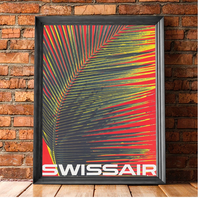 May include: Framed vintage Swissair travel poster. The poster features a large palm leaf in yellow and dark gray against a red background. The word "SWISSAIR" is printed in white at the bottom of the poster. The poster is in a black frame.