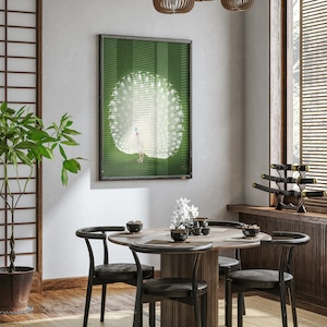 Op de afbeelding: Een ronde houten eettafel met vier zwarte stoelen. De tafel is gedekt met vier kommen en een vaas met witte bloemen. Een ingelijst afdruk van een witte pauw met zijn staartveren uitgespreid hangt aan de muur achter de tafel.