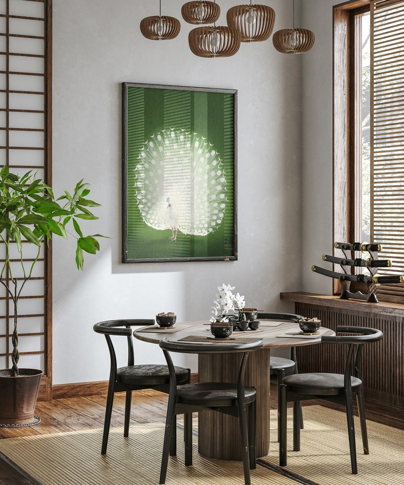 Op de afbeelding: Een ronde houten eettafel met vier zwarte stoelen. De tafel is gedekt met vier kommen en een vaas met witte bloemen. Een ingelijst afdruk van een witte pauw met zijn staartveren uitgespreid hangt aan de muur achter de tafel.