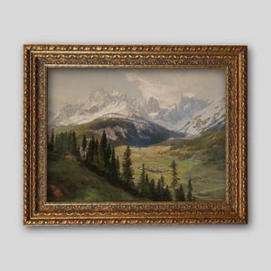 Op de afbeelding: Een landschapsschilderij in een decoratieve gouden lijst met een bergketen met besneeuwde toppen, een groene vallei en een groep bomen op de voorgrond. De sc&egrave;ne toont een kleine hut verscholen tussen de donkergroene dennenbomen.