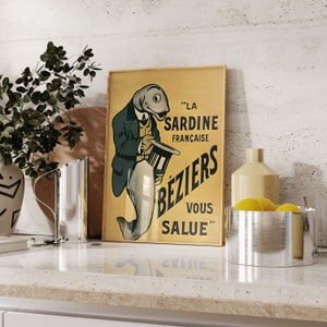 K&ouml;nnte beinhalten: Ein rechteckiges gerahmtes Poster mit gelbem Hintergrund zeigt eine Illustration eines Fisches in einem Anzug, der einen Zylinder h&auml;lt. Der Text lautet: LA SARDINE FRAN&Ccedil;AISE B&Eacute;ZIERS VOUS SALUE. Das Poster steht in einer K&uuml;chenumgebung.