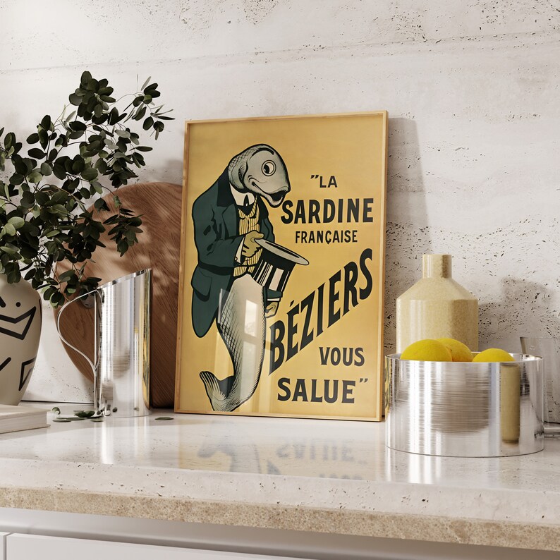 K&ouml;nnte beinhalten: Ein rechteckiges gerahmtes Poster mit gelbem Hintergrund zeigt eine Illustration eines Fisches in einem Anzug, der einen Zylinder h&auml;lt. Der Text lautet: LA SARDINE FRAN&Ccedil;AISE B&Eacute;ZIERS VOUS SALUE. Das Poster steht in einer K&uuml;chenumgebung.