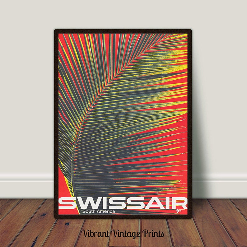 May include: A framed vintage travel poster featuring a palm leaf against a red background. The poster has the text "SWISSAIR South America" in white and a small airplane graphic. The poster is in a black frame.