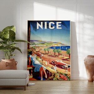 Puede incluir: Un p&oacute;ster de viaje vintage enmarcado para Niza, Francia, que presenta una escena costera con palmeras, coches cl&aacute;sicos y una mujer con un vestido azul. La palabra "NICE" se muestra en la parte superior. El p&oacute;ster est&aacute; colocado contra una pared blanca con una planta y jarrones decorativos.