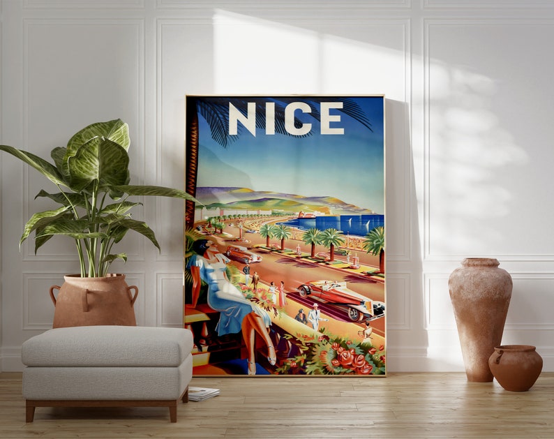 Puede incluir: Un p&oacute;ster de viaje vintage enmarcado para Niza, Francia, que presenta una escena costera con palmeras, coches cl&aacute;sicos y una mujer con un vestido azul. La palabra "NICE" se muestra en la parte superior. El p&oacute;ster est&aacute; colocado contra una pared blanca con una planta y jarrones decorativos.