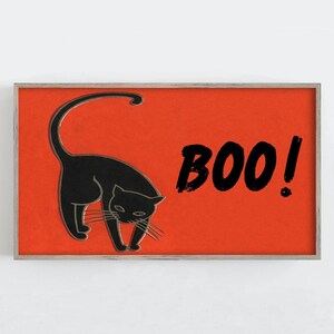 May include: A framed Halloween-themed print featuring a black cat with an arched back on a bright orange background. The word "BOO!" is written in black brushstrokes. The print has a silver frame.