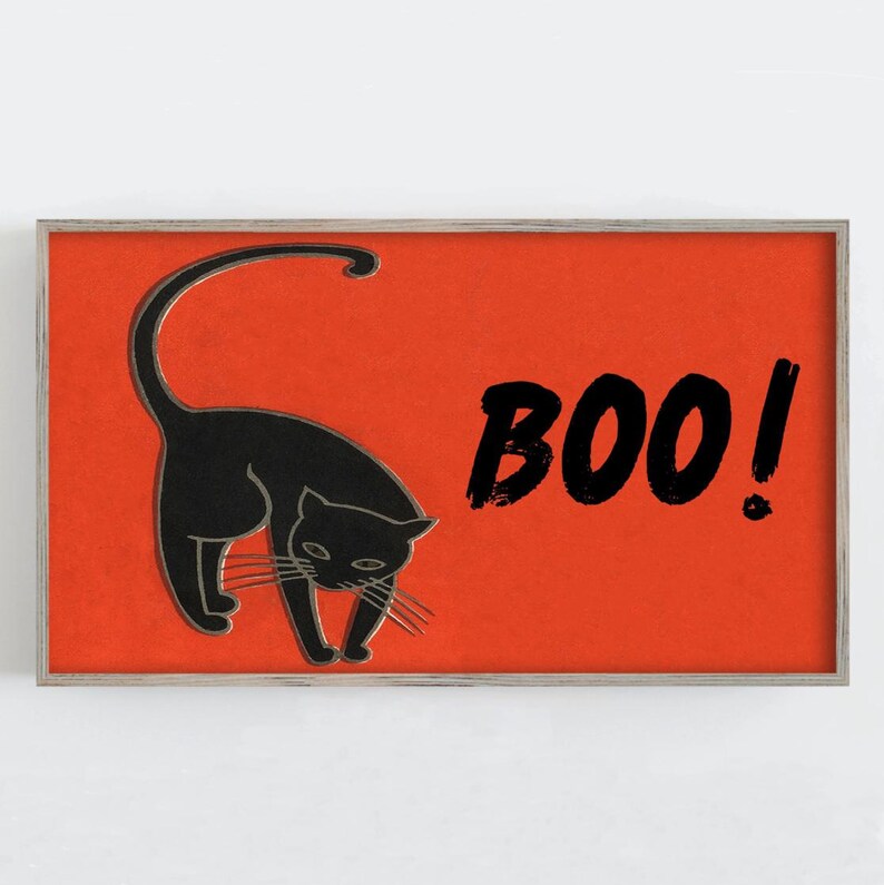 May include: A framed Halloween-themed print featuring a black cat with an arched back on a bright orange background. The word "BOO!" is written in black brushstrokes. The print has a silver frame.
