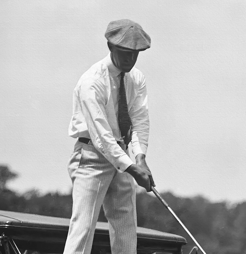 Op de afbeelding: Een man in een wit overhemd, een gestreepte das en een pet houdt een golfclub vast. Hij staat op een golfbaan.