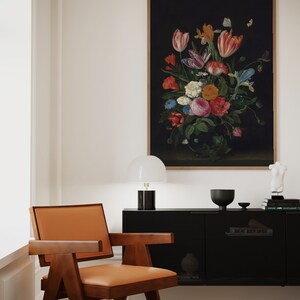 K&ouml;nnte beinhalten: Ein gerahmtes Stillleben mit Blumen vor dunklem Hintergrund h&auml;ngt &uuml;ber einem schwarzen Schrank. Das Gem&auml;lde zeigt einen Strau&szlig; bunter Blumen, darunter Tulpen und Rosen. Ein Stuhl im Mid-Century-Modern-Stil mit braunem Holzrahmen und hellbraunem Ledersitz steht vor dem Schrank.