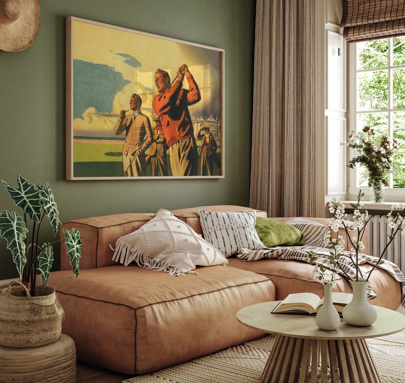 Pu&ograve; includere: Un poster vintage di tre uomini che giocano a golf su un campo verde. Il poster &egrave; incorniciato e appeso a una parete verde in un soggiorno con un divano in pelle marrone e un tavolino da caff&egrave;.