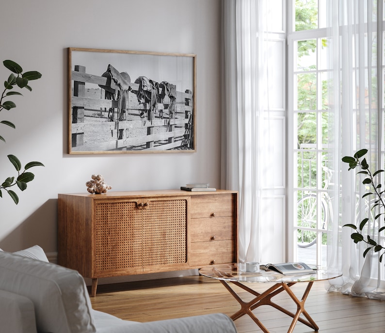 K&ouml;nnte beinhalten: Ein Wohnzimmer im Stil der Mid-Century Modern mit einem Schrank aus Holz mit einer geflochtenen Rattan-T&uuml;r, einem Glas-Couchtisch und einem Schwarzwei&szlig;foto von Pferden, das an der Wand h&auml;ngt.