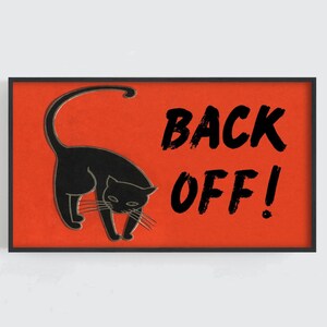 May include: A framed art print featuring a black cat silhouette on a vibrant orange background. Bold black text reads "BACK OFF!" The artwork has a vintage, slightly distressed aesthetic, perfect for adding a touch of humor to any space.