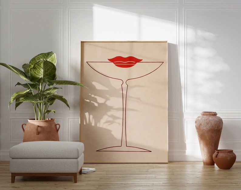 May include: A rectangular framed wall art print featuring a minimalist dark red line drawing of a martini glass centred on a light beige background. A pair of bold, solid red lips is positioned directly above the rim of the glass.